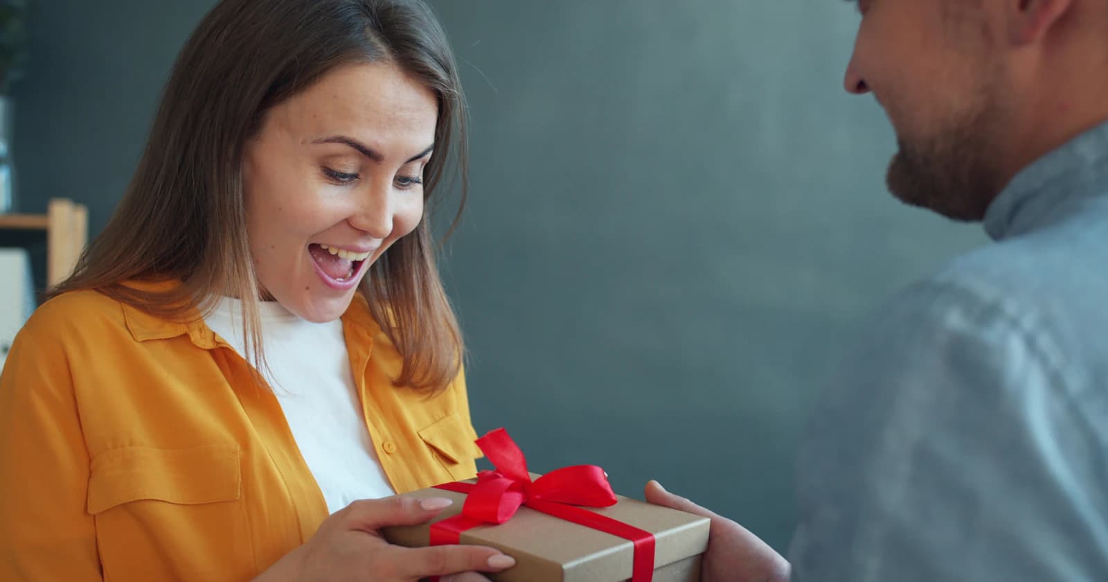 A woman smiling as her partner gives her a carefully wrapped gift