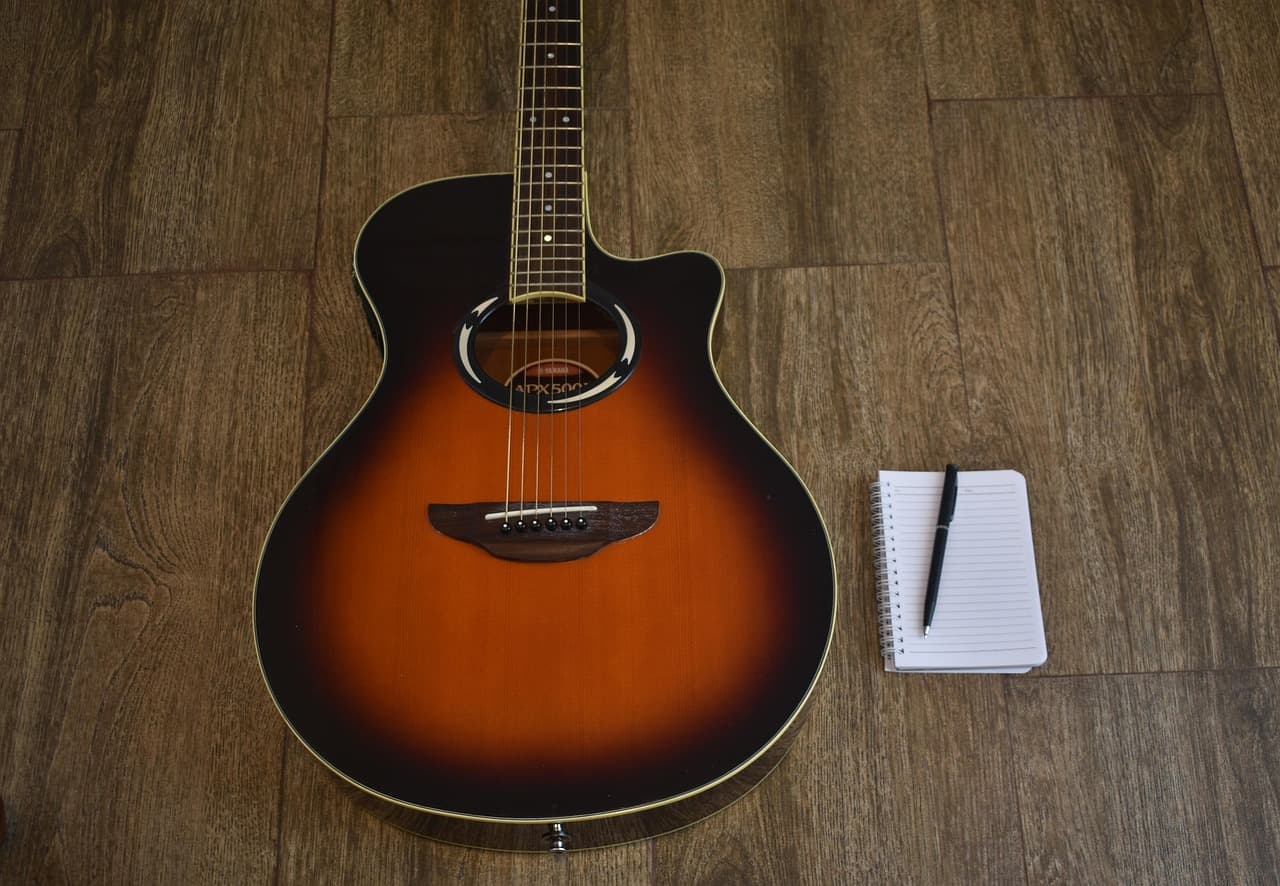 A songwriter's notebook filled with handwritten lyrics, sitting next to an acoustic guitar